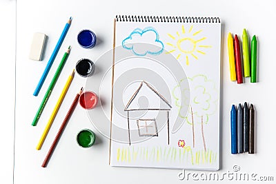 Pencils and brushes lying around scketchbook with kids crayon drawing Stock Photo
