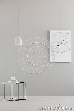 Pendant light above a modern table and a city map poster on a gray wall in a minimalist living room interior and place for a sofa. Stock Photo