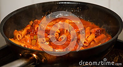 Penne pasta cooking in fresh homemade tomato sauce with zucchini and sun dried tomatoes - Real food cooking concept. Delicious cor Stock Photo