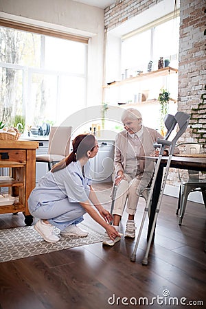 Pensioner smiling while caregiver lacing shoes for her Stock Photo