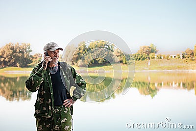 pensioner talks on phone on vacation, fisherman, Internet in nature, communication with friends, relatives. copy space Stock Photo