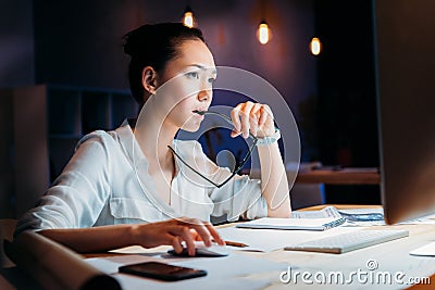 Pensive asian businesswoman holding eyeglasses and looking at computer monitor Stock Photo