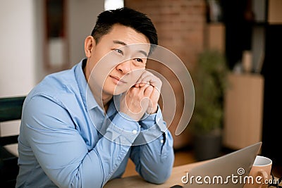 Pensive asian middle aged male freelancer thinking about something, working on laptop at home, copy space Stock Photo