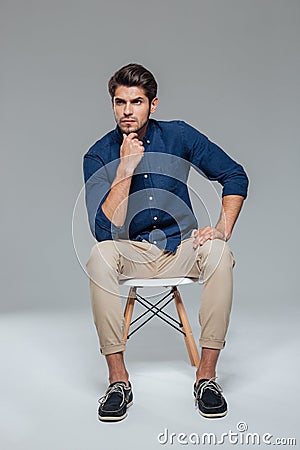 Pensive attractive casual young man sitting on chair Stock Photo
