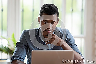 Pensive biracial male employee work on laptop thinking Stock Photo