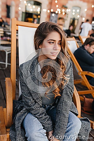 Pensive blue-eyed girl with pale skin sitting in recliner in outdoor cafe and looking away. Shy brunette caucasian woman Stock Photo