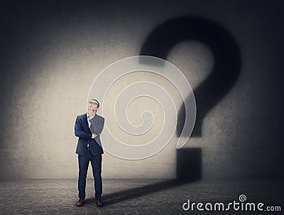 Pensive businessman casting an interrogation mark shadow on the wall. Business questions and decision making concept. Thinking and Stock Photo