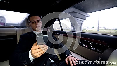 Pensive businessman writing e-mail, riding in car, stressful job, workaholic Stock Photo