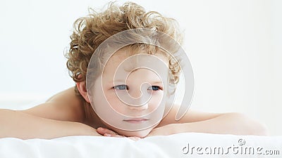 Pensive curly-haired boy lying in bed. Stock Photo