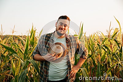 Pensive farmer smiles on face stand in field, took off hat, tired, front view, looking at camera. Stock Photo