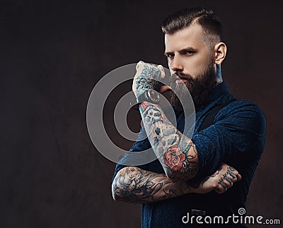 Pensive handsome old-fashioned hipster in a blue shirt and suspenders, standing with hand on chin in a studio. Stock Photo