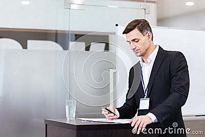 Pensive handsome speaker using mobile phone standing at tribune Stock Photo