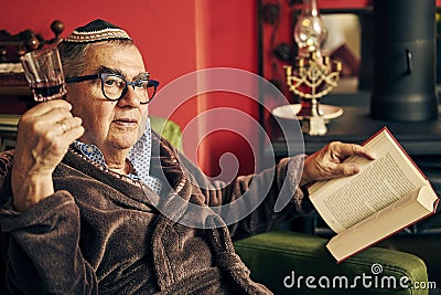 Pensive Jewish senior reading a torah book and drinking kosher wine Stock Photo