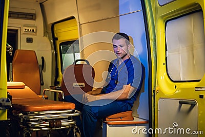 A pensive medical worker in a blue uniform sitting inside the ambulance car and meditating Stock Photo