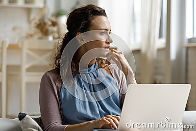 Pensive millennial remote employee woman distracting from work at laptop Stock Photo