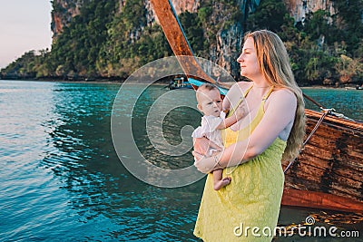 Pensive mother with a disgruntled baby stand on the pier against the background of water in the early morning and meet sunrise in Stock Photo