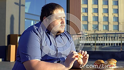 Pensive obese man eating burger, hesitating to start new life, weight loss Stock Photo
