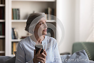 Pensive positive senior smartphone user woman sitting on home couch Stock Photo