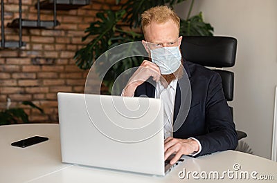 Pensive red-haired businessman in smart casual suit wearing protective face mask Stock Photo