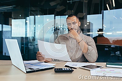 Pensive serious businessman reading financial report, hispanic businessman holding document in hands looking Stock Photo