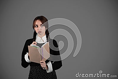 Pensive smart young girl student in gothic black clothes with pigtails with book, got idea and look at empty space Stock Photo