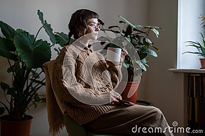 Thoughtful teen girl with cup of tea and smartphone looking at window, thinking of life, relations Stock Photo