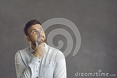 Pensive thoughtful caucasian bearded man touching chin looks up studio shot Stock Photo