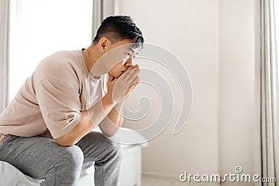 Pensive thoughtful mature asian man wearing pajamas sitting on bed Stock Photo