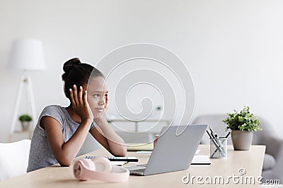 Pensive tired bored adolescent afro american girl studying remotely, rest from lesson and looking at laptop Stock Photo