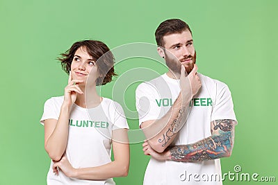 Pensive two young friends couple in white volunteer t-shirt isolated on green background. Voluntary free work assistance Stock Photo