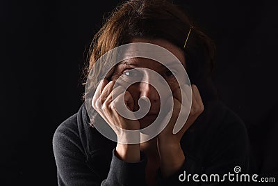 Pensive woman with both hands on her face looking at camera on black Stock Photo
