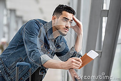 Pensive Young Middle Eastern Man With Passport And Tickets Standing In Airport Stock Photo