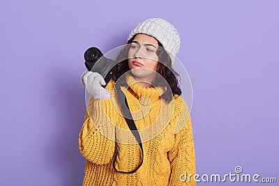 Pensive young pretty european girl photographer using modern camera, looking thoughtfully at camera, being puzzled and upset, Stock Photo