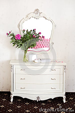 Peony flowers on a white commode under a mirror Stock Photo