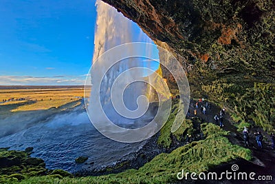 People admiring a majestic waterfall, standing on the side of a rocky cliff, Iceland, Reykjavik Stock Photo