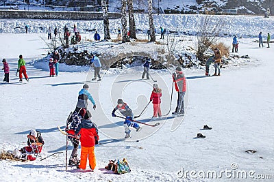 People of all age groups enjoying sunny day, skating and playing ice hockey on a frozen lake, when temperatures drop on winter. Editorial Stock Photo