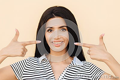 People, beauty and advertising concept. Brunette young woman with gentle smile, indicates at mouth with broad smile, has braces, w Stock Photo