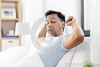 Sleepy indian man stretching in bed at home Stock Photo