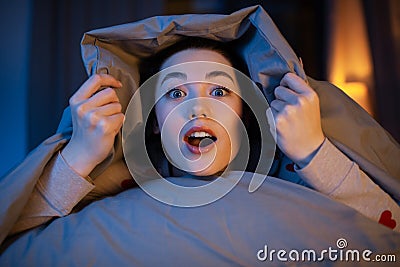 surprised teenage girl under blanket in bed Stock Photo