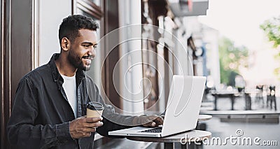 People city lifestyle young man sitting in a cafe using his laptop computer typing keyboard online outside Stock Photo