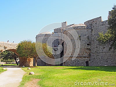 People crossing the amboise gate in the medieval walls of the old city in rhodes town surrounded by grass and trees Editorial Stock Photo