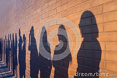 People crowd shadows lined up against a red brick wall. They are in a queue for changes in life. Social distance, covid Stock Photo