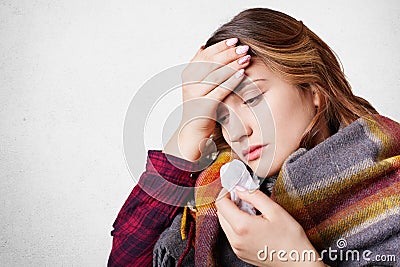 People, disease, healthcare concept. Stressful woman has flu, suffers from running nose, bad cold and headache, wrapped in wool pl Stock Photo