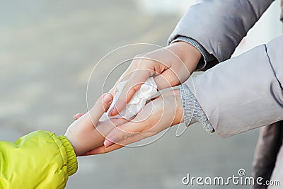 People disinfecting hands with antiseptic wet wipe outdoors. Woman cleaning kid hands with antiseptic tissue outdoors Stock Photo