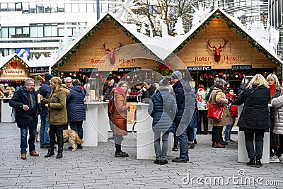 People on Cmarket in front of stalls with mulled wine, punch at Dusseldorf Christmas market. Village in front of modern buildings Editorial Stock Photo