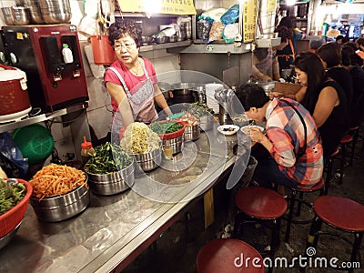 People eating in front of the cook in a restaurant in an alley of Namdaemun market. Seoul Editorial Stock Photo