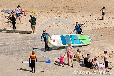 People enjoying the beach, stand up paddleboarders with board. Cullercoats Bay, North Tyneside, UK Editorial Stock Photo