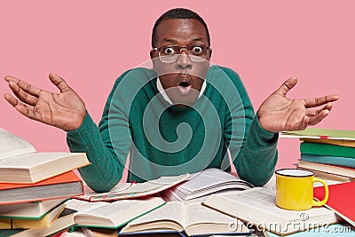 People, exam preparation and studying concept. Puzzled dark skinned wonk demonstrates hesitation gesture, looks in Stock Photo