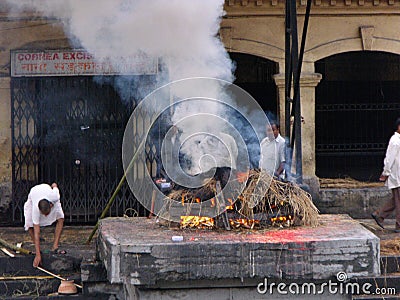 People by the fire of a funeral pyre with a corpse being cremated at the Pashupatinath temple in Kathmandu, Nepal Editorial Stock Photo