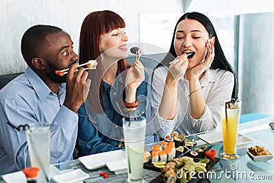 People, food, fun, sushi meal. Close up shot of excited hungry funny three multiethnical friends, having fun at cafe Stock Photo